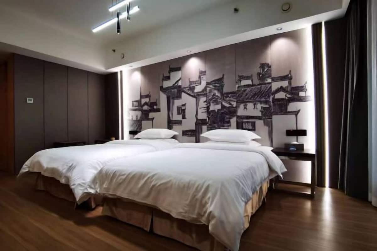 A modern hotel room with a large bed, wooden flooring, and a wall mural of traditional architecture.
