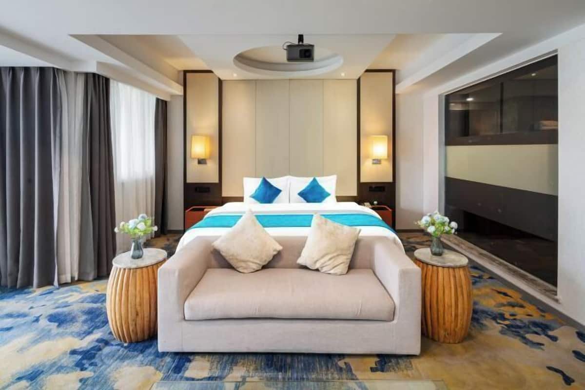 A modern hotel room with a large bed, a sofa, two side tables, and a ceiling projector.