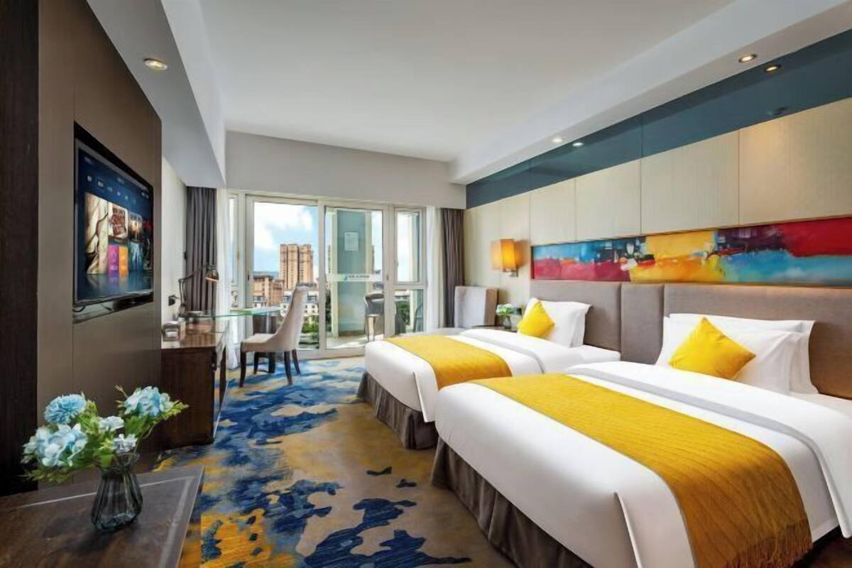 A hotel room with two beds, a desk, a TV, and a large window.