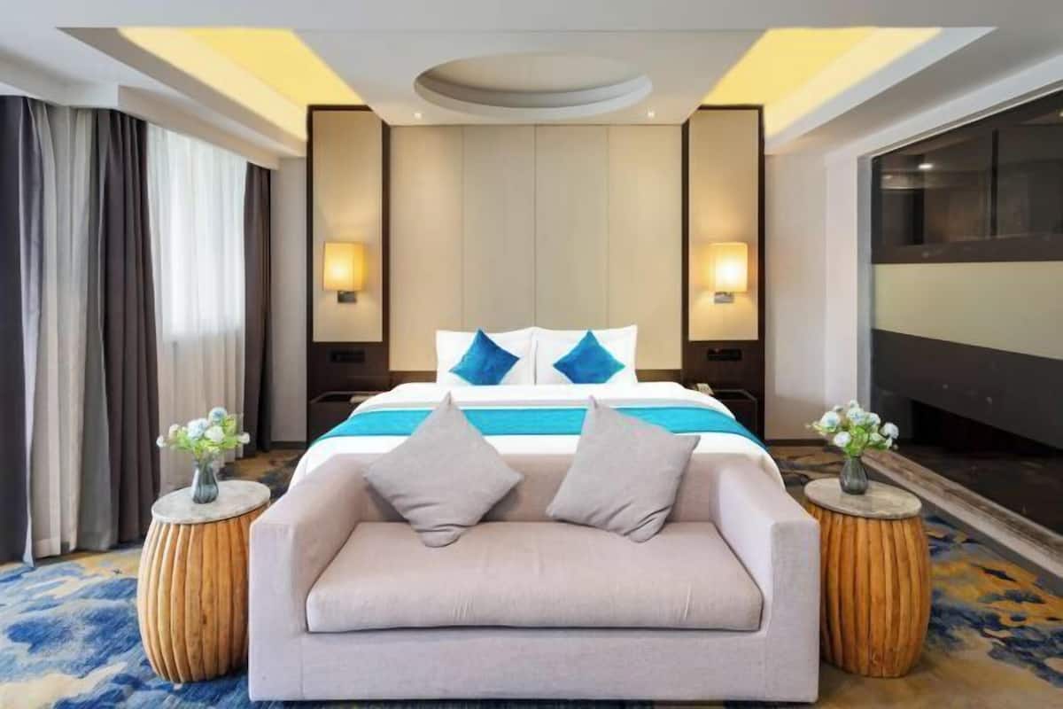 A hotel room with a bed, a sofa, two side tables, and a large window.
