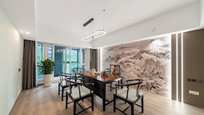 A modern dining area with a wooden table and chairs, a large window with curtains, and a wall mural. - LiSheng Yijia Hotel (Chengdu)