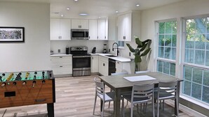 Una cocina moderna con armarios blancos, electrodomésticos de acero inoxidable y un comedor con mesa y sillas.