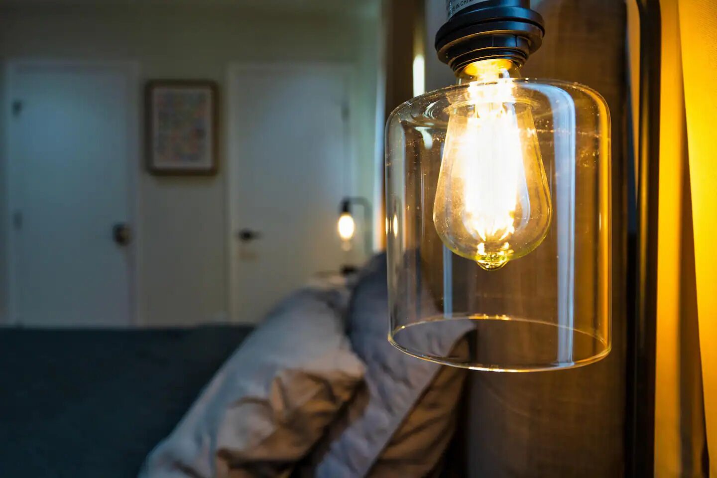 A room with a bed, pillows, and a hanging light fixture.