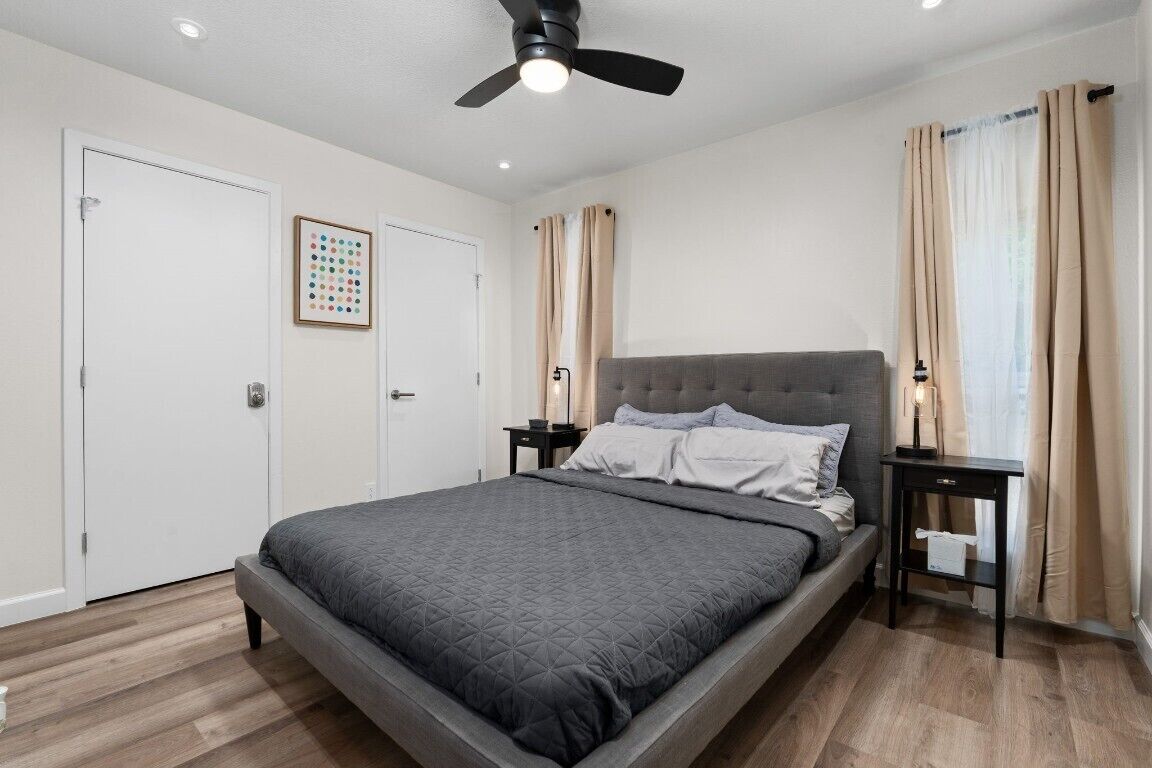 A bedroom with a bed, a ceiling fan, a nightstand, and a door.