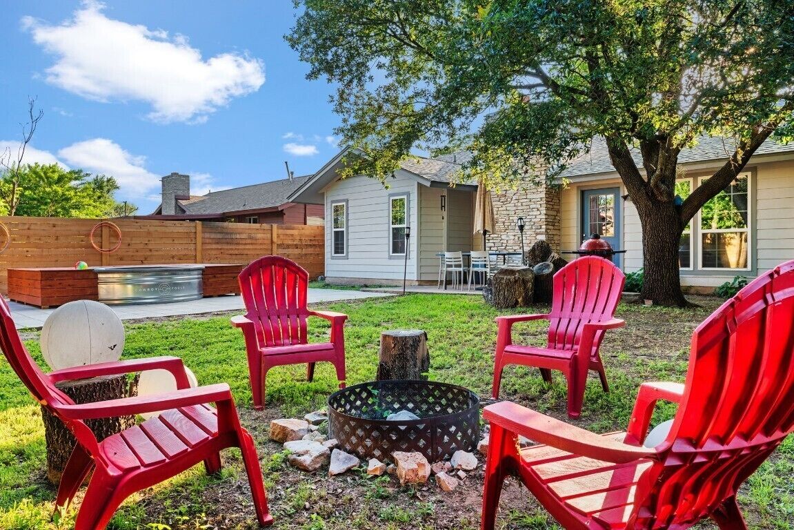 A backyard with a fire pit, red Adirondack chairs, and a wooden deck.