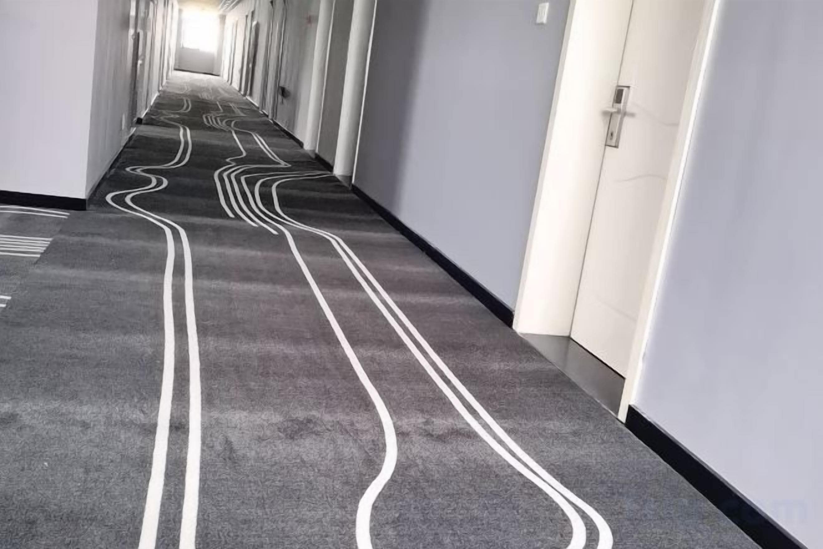 A corridor with a patterned carpet and white lines on the floor, leading to a door.