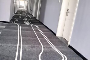 Ein Korridor mit einem gemusterten Teppich und weißen Linien auf dem Boden, der zu einer Tür führt.