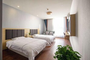 Ein modernes Hotelzimmer mit zwei Betten, einem Schreibtisch, einem Sessel, einem Fernseher und einem großen Fenster mit Vorhängen.