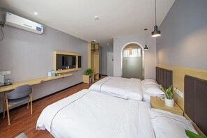 Ein Hotelzimmer mit zwei Betten, einem Schreibtisch, einem Stuhl, einem Fernseher und einer kleinen Pflanze.