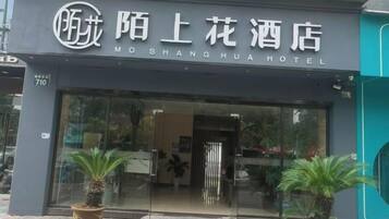 A hotel entrance with a sign in a foreign language, a glass door, and potted plants in front.