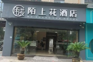 Entrada de hotel con un letrero en idioma extranjero, puerta de vidrio y plantas en macetas.