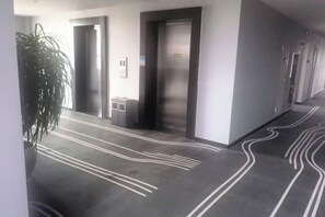 A hallway with doors, a plant, and a patterned floor. - Haining Stranger Shanghua Hotel (Haining)