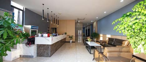 A modern hotel lobby with a reception desk, seating area, and a large plant.