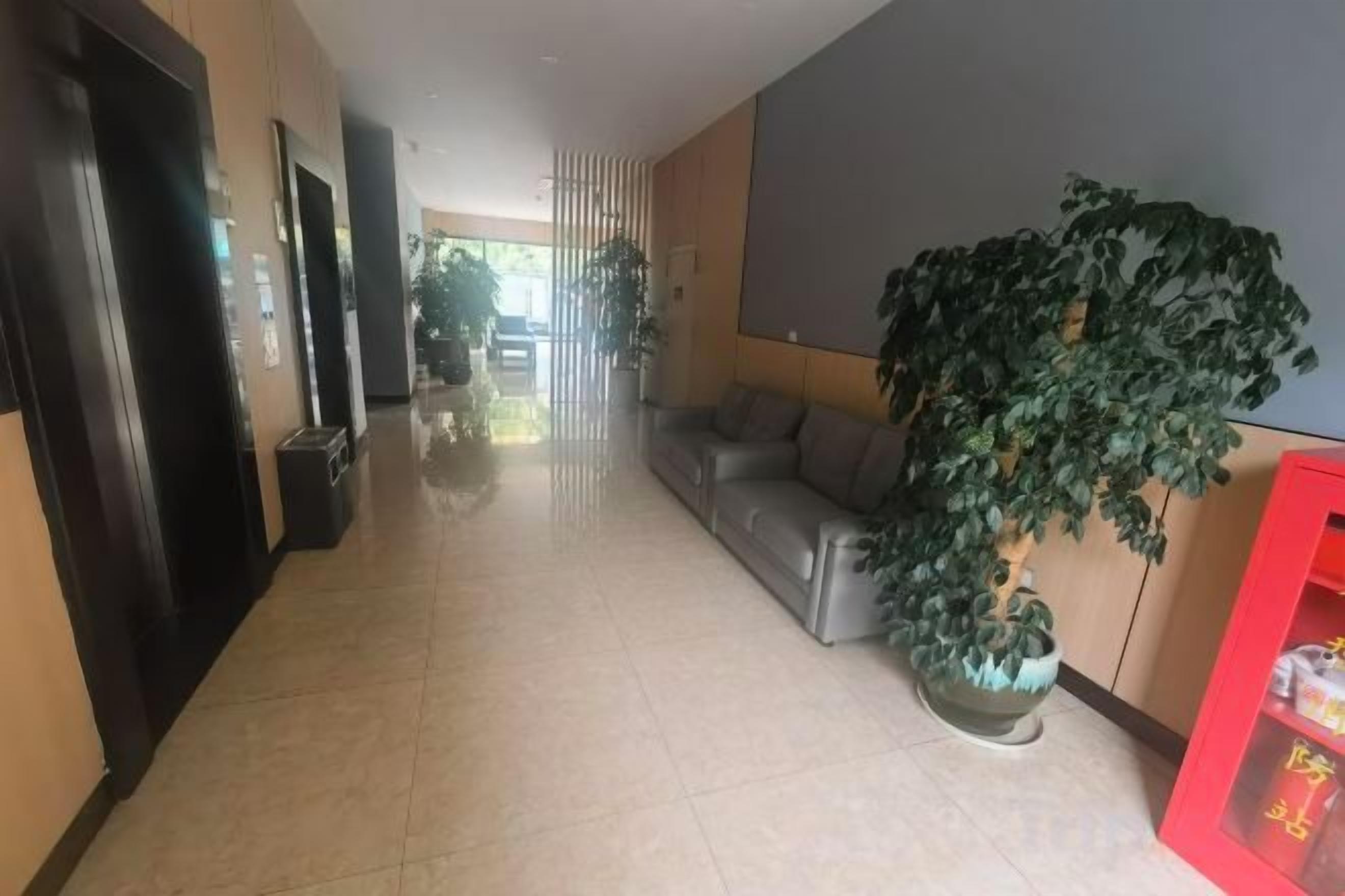 Un corridoio d'hotel con una reception, una zona relax e un'ampia pianta in vaso.