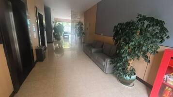 Un corridoio d'hotel con una reception, una zona relax e un'ampia pianta in vaso.
