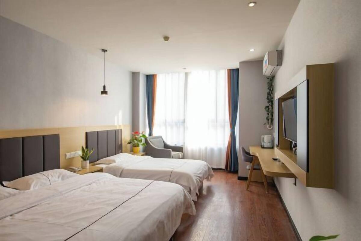 A hotel room with two beds, a desk, a chair, a TV, and a window with curtains.