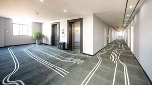 A modern hotel corridor with a patterned carpet, elevators, and a potted plant. - Haining Stranger Shanghua Hotel (Haining)
