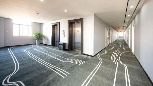 A modern hotel corridor with a patterned carpet, elevators, and a potted plant. - Haining Stranger Shanghua Hotel (Haining)
