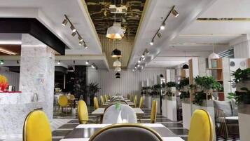 A modern dining area with long tables and yellow chairs, featuring a marble column and pendant lighting.
