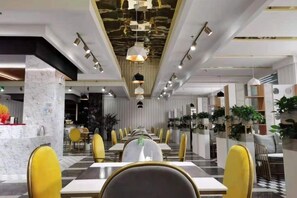 Zona pranzo moderna con lunghe tavolate e sedie gialle, arricchita da una colonna in marmo e illuminazione a sospensione.