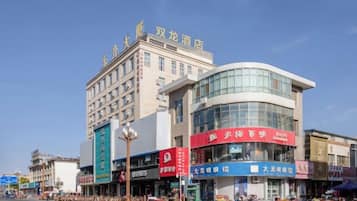A multi-story hotel with a curved glass facade, multiple ground-level shops, and a clear blue sky.