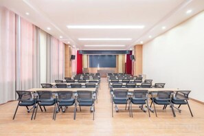 A conference room with rows of tables and chairs, a stage with a screen, and a large window on one side. - Shuang Long Hotel (Gaotai)