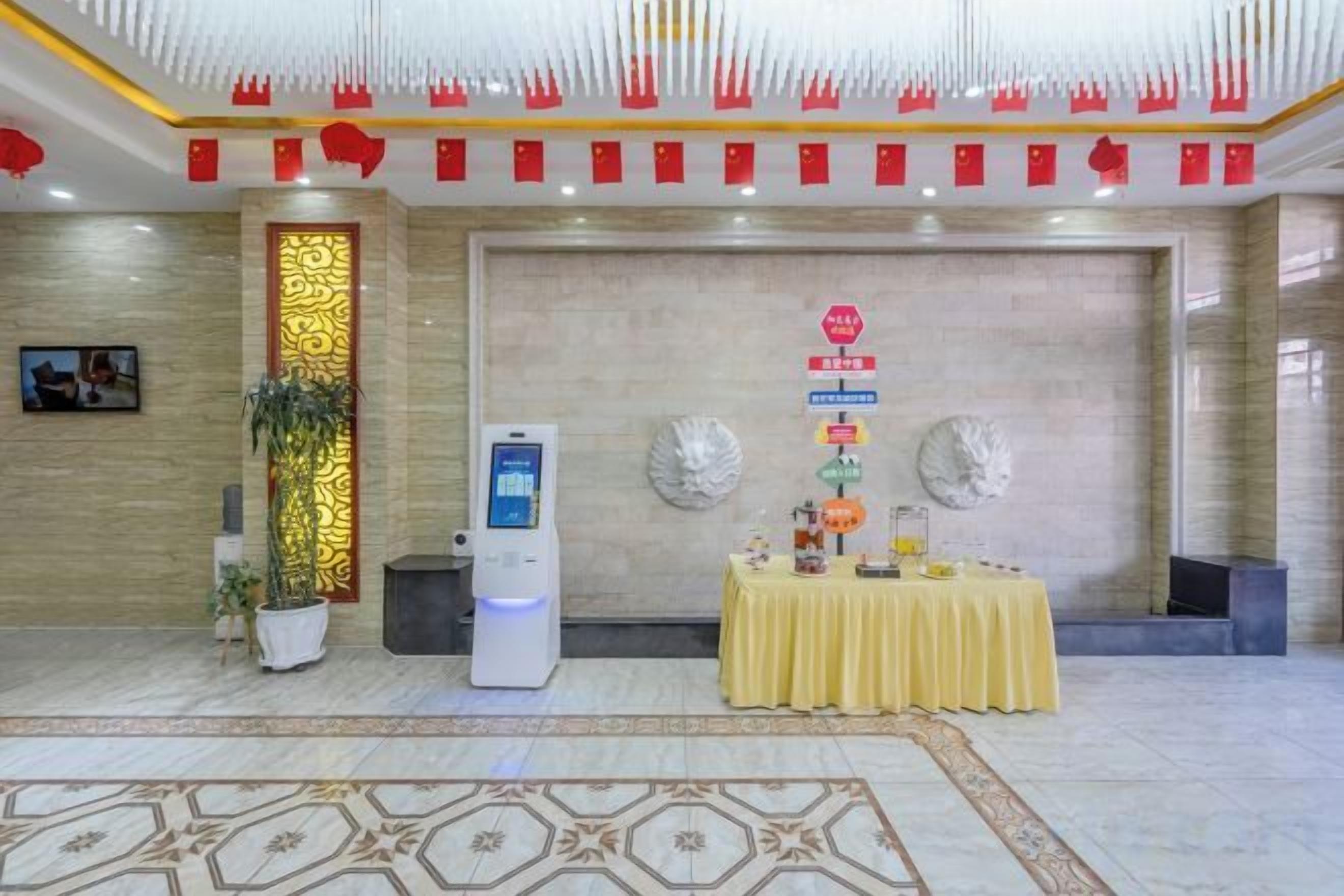 A hotel lobby with a reception desk, a self-service kiosk, and a decorative table with a yellow tablecloth.