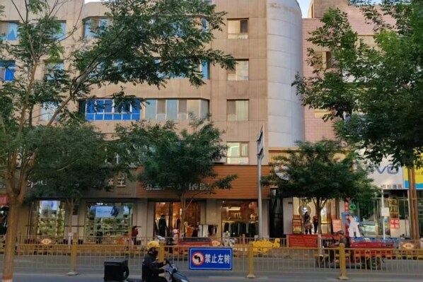 Un immeuble à plusieurs étages doté d’une façade moderne, une zone piétonne agrémentée d’arbres et un panneau indiquant une zone où le stationnement est interdit.