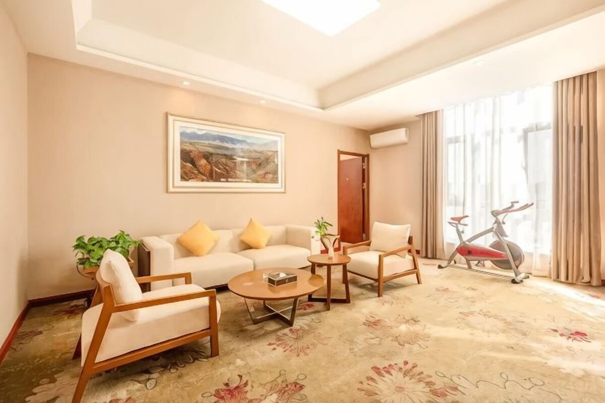 A hotel room with a sofa set, a coffee table, a bicycle, and a large window with curtains.