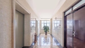 A hallway with a polished marble floor, a potted plant, and a dark wooden door. - Shuang Long Hotel (Gaotai)