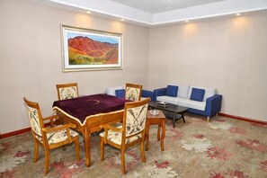 A dining area with a table and chairs, a sofa, and a painting on the wall. - Shuang Long Hotel (Gaotai)