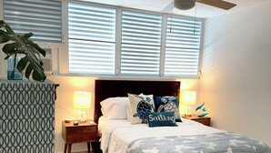A bedroom with a bed, bedside lamps, a ceiling fan, and a window with blinds. - Oceanview Apartment by Playa Azul - walk to shore, snorkel, swim, sun, unwind. (Luquillo)