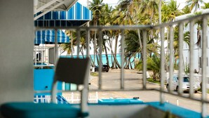 A view from a balcony with a railing, overlooking a street lined with palm trees and parked cars. - Oceanview Apartment by Playa Azul - walk to shore, snorkel, swim, sun, unwind. (Luquillo)