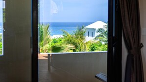 A view from a balcony overlooking a beach with palm trees and a white building in the distance. - 6BR Boutique Hotel in Punta Sur (Isla Mujeres)