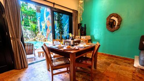 A dining area with a wooden table, chairs, and a view of a pool and garden through large glass doors. - 6BR Boutique Hotel in Punta Sur (Isla Mujeres)