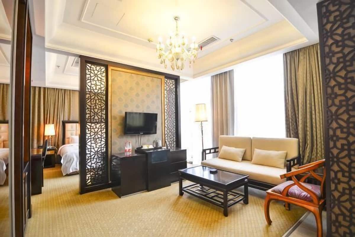 Ein Hotelzimmer mit einer Couch, einem Couchtisch, einem Fernseher und einem dekorativen Raumteiler.