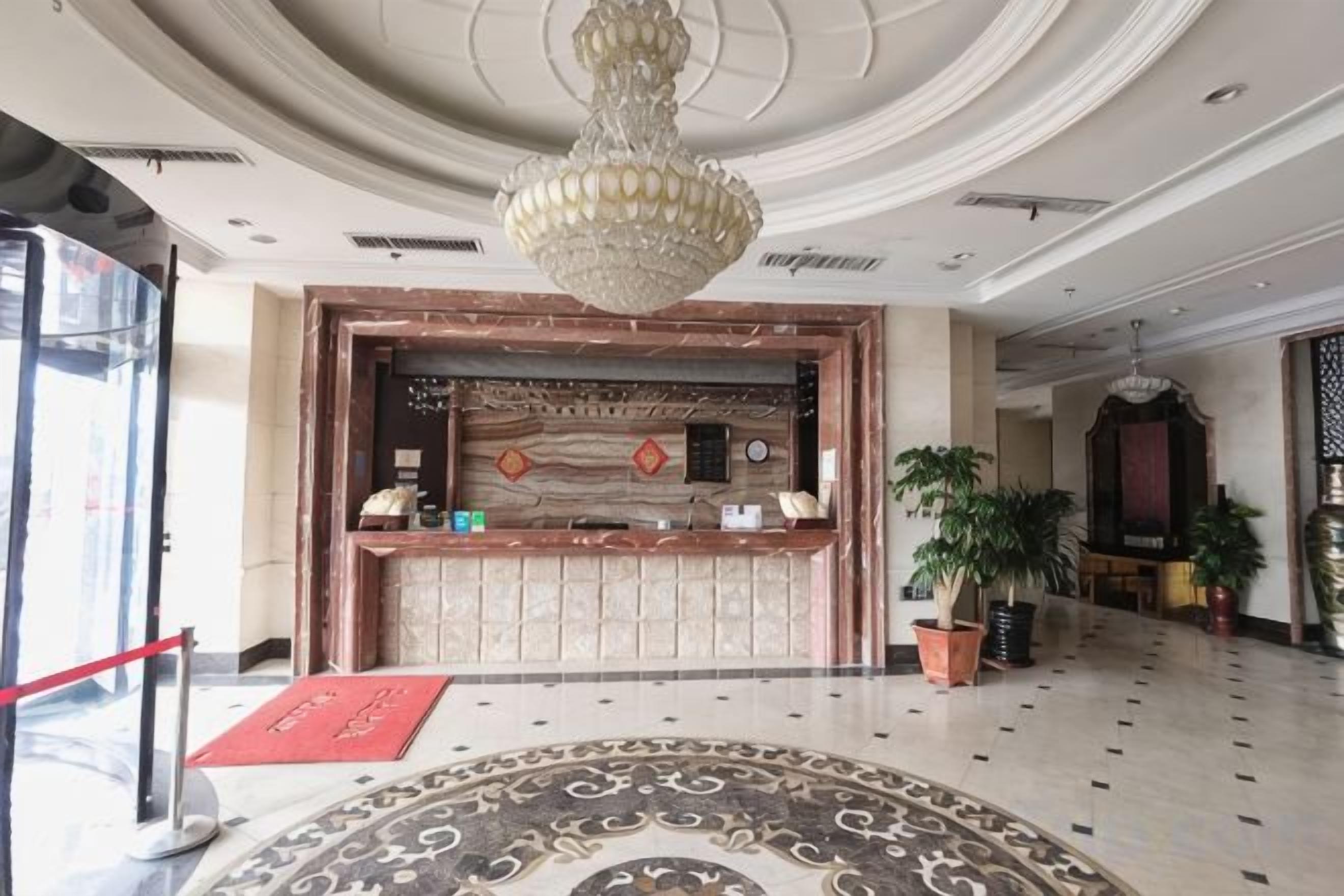 Un hall de hotel con una recepción, una araña de cristal y plantas en macetas.