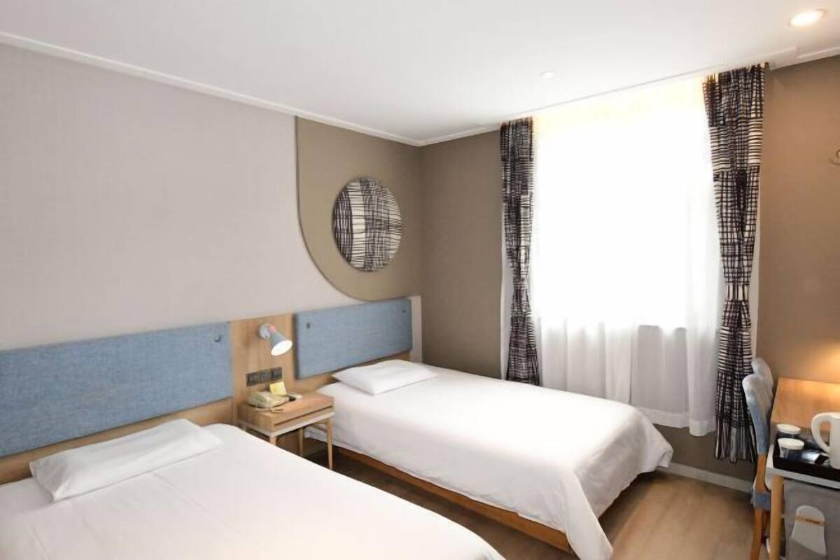 Habitación de hotel con dos camas, un adorno circular en la pared, un escritorio con una silla y una ventana con cortinas.
