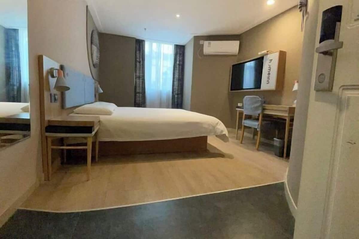 Una habitación de hotel con cama, escritorio, silla, televisor y aire acondicionado.