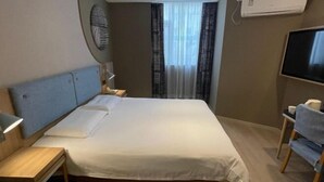 A hotel room with a bed, bedside table, lamp, TV, and a window with curtains.