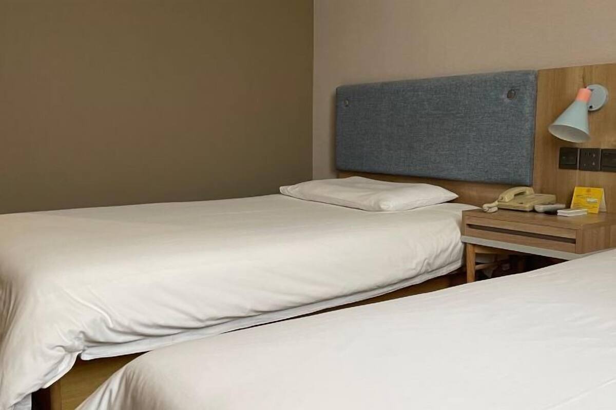Una habitación de hotel con dos camas individuales, una mesita de noche de madera con lámpara, teléfono y una pequeña mesa.