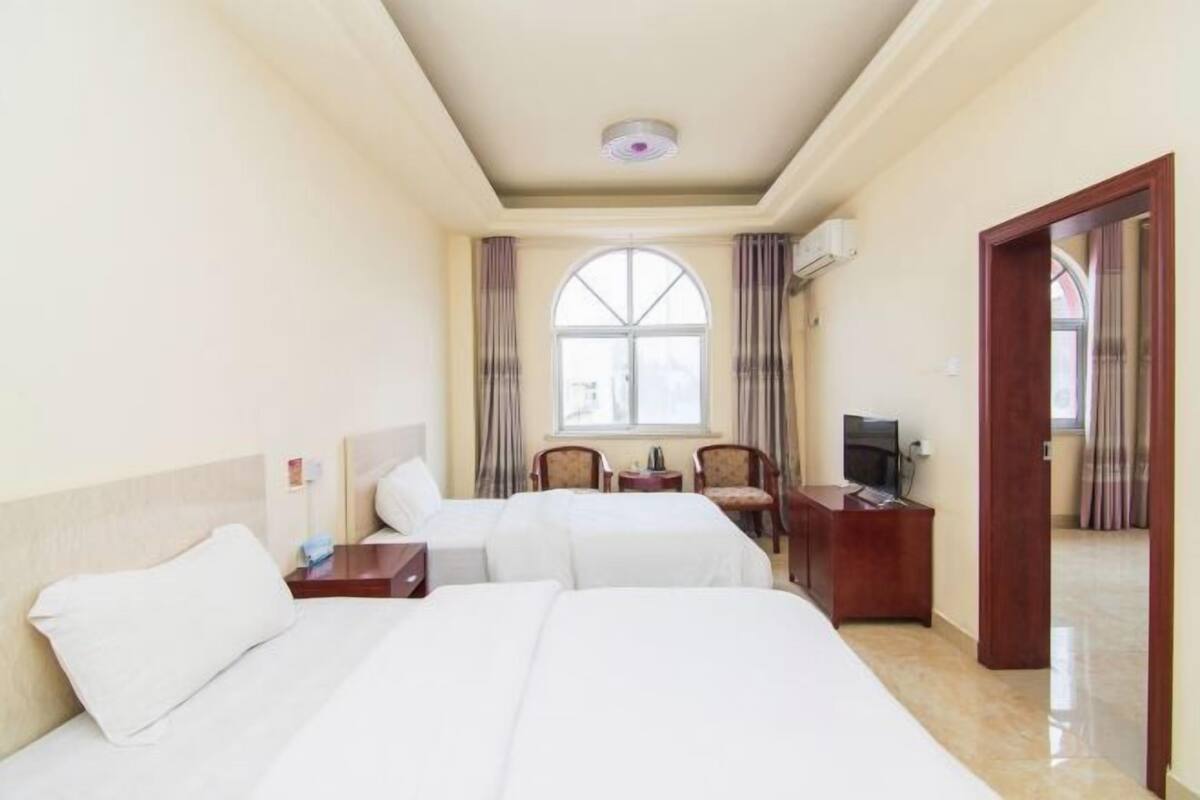 A hotel room with two beds, a TV, a desk, and a window with curtains.
