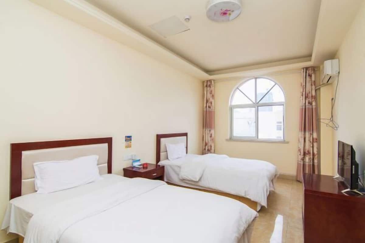 A hotel room with two beds, a TV, and a window with curtains.