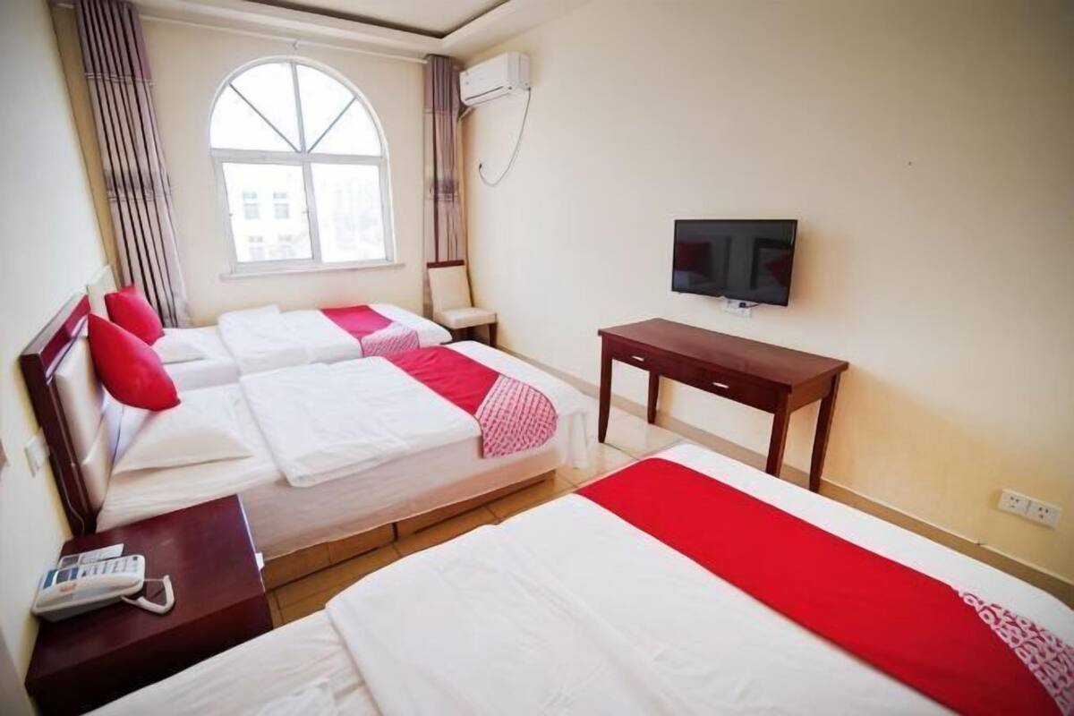 A hotel room with two beds, a TV, a desk, and a window.