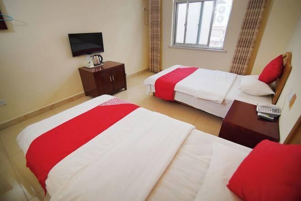 A hotel room with two beds, a TV on the wall, and a window with curtains.