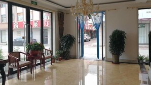 Un hall d’hôtel agrémenté d ’un lustre, de plantes en pot et offrant une vue sur la rue à travers de grandes portes vitrées.