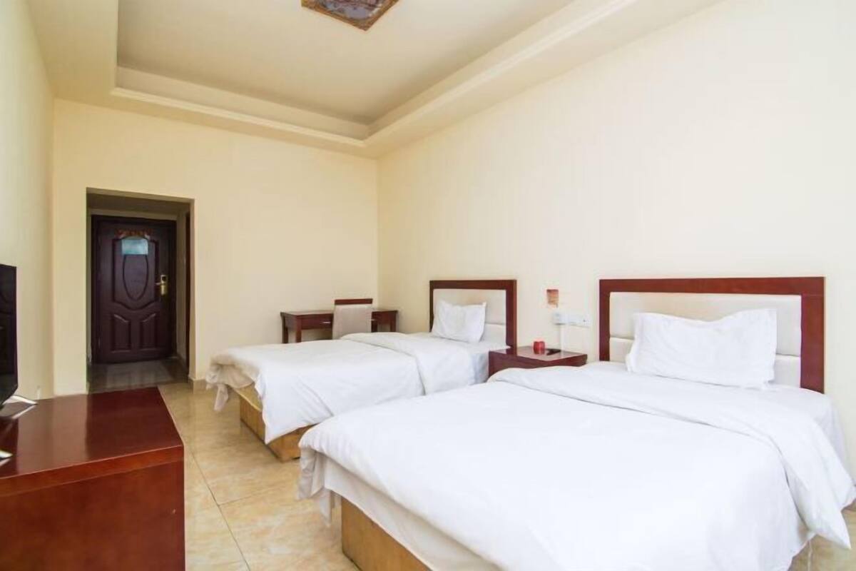 A hotel room with two single beds, a wooden desk, a TV, and a door.