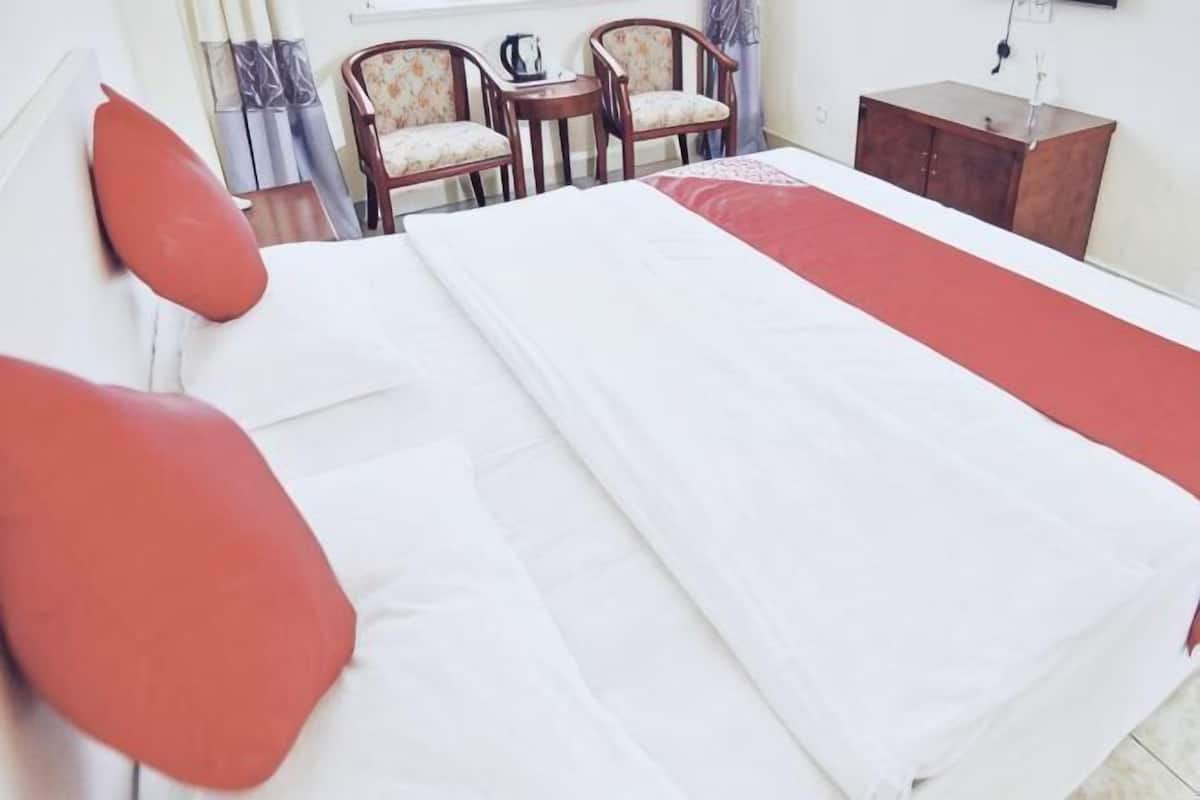 A hotel room with a bed, two chairs, a small table, and a cabinet.