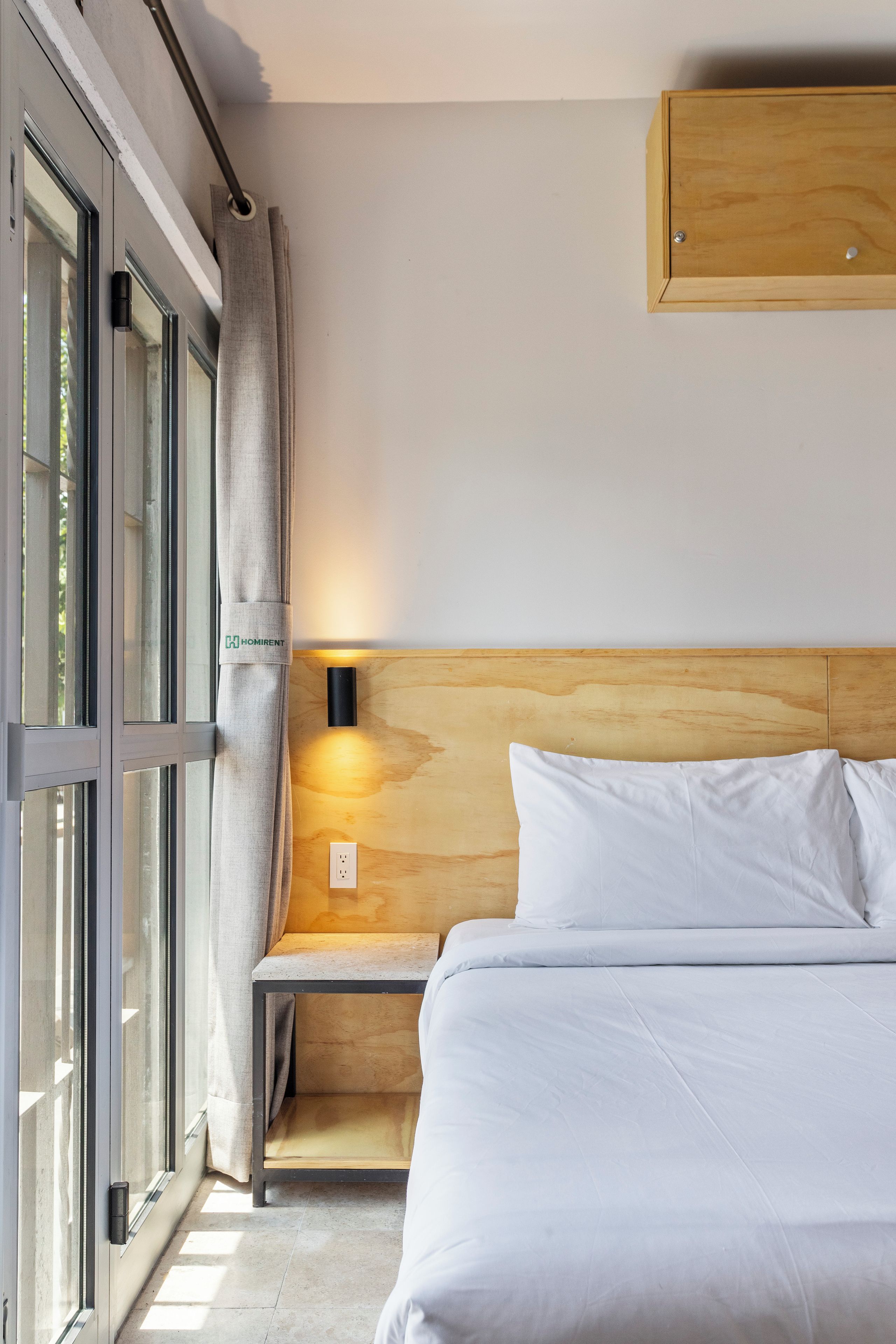 Ein Schlafzimmer mit einem Bett, einem Nachttisch, einer Wandleuchte und einem fenster mit Vorhängen.