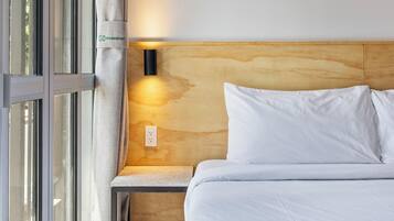 A bedroom with a bed, a nightstand, a wall-mounted light, and a window with curtains.